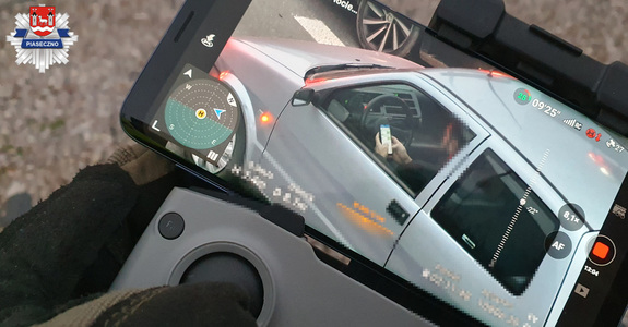 Kierujący siedzącą za kierownicą pojazdu, w trakcie jego prowadzenia trzyma telefon w ręku, pisząc wiadomości smsowe