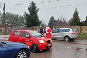 Policjanci kontrolują pojazd wspólnie z mikołajem, który wręcza prezent za przepisową jazdę