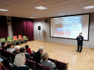 Policjantka stoi przed seniorami, na ekranie wyświetlana jest prezentacja