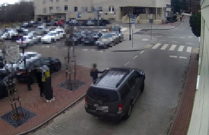 Zdjęcie z kamery monitoringu, pojazd marki nissan jadący drogą, na belce pojazdu kobieta trzymająca się ręką za reling dachowy