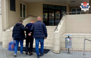 Zatrzymany mężczyzna z kajdankami na rękach prowadzony przez dw,och nieumundurowanych policjantów