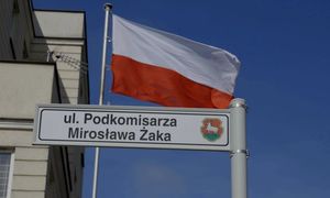 powiewająca flaga Polski, tabliczka z nazwą ulicy &quot;podkomisarza Mirosława Żaka&quot;