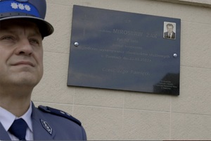 tablica Mirosława Żaka, a w tle stojący policjant