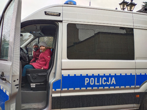 Dziewczynki ubrane w kurtki siedzą w policyjnym radiowozie za kierownicą.