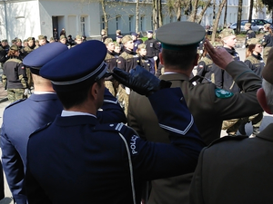 Na zdjęciu tyłem stoją umundurowani policjanci wraz z funkcjonariuszami innych służb. Wszyscy oddają honor.