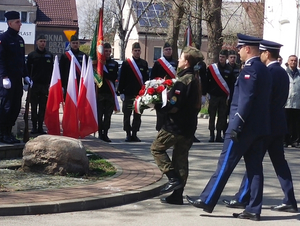 Na zdjęciu idą umundurowani policjanci a przed nimi uczeń szkoły wojskowej niosący wiązankę kwiatów.