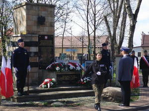 Na zdjęciu umundurowany policjant stoi na baczność przed pomnikiem.