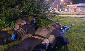 dwóch policjantów w strojach bojowych leżący na trawie z bronią