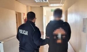 zatrzymany mężczyzna w asyście umundurowanego policjanta, obydwaj stoją tyłem