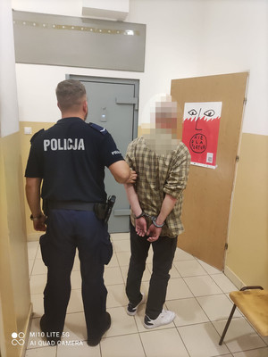 mężczyzna w asyście umundurowanego policjanta, stoją tyłem