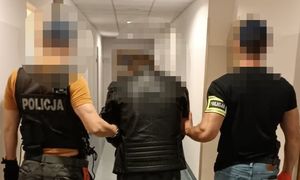 zatrzymany mężczyzna wraz z dwoma nieumundurowanymi policjantami, stoją tyłem na korytarzu komendy