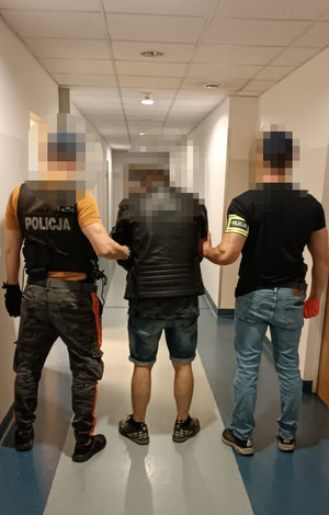 zatrzymany mężczyzna wraz z dwoma nieumundurowanymi policjantami, stoją tyłem na korytarzu komendy
