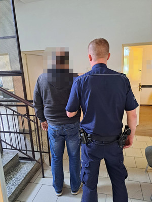 zatrzymany mężczyzna z umundurowanym policjantem na korytarzu obok klatki schodowej