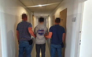 nieumundurowani policjanci wraz z zatrzymanym nastolatkiem, stoją tyłem na korytarzu