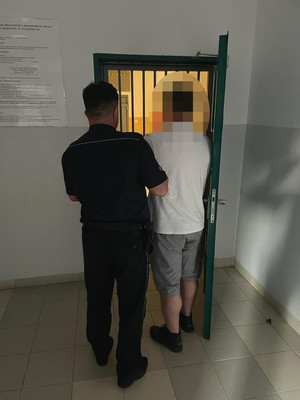 zatrzymany mężczyzna wraz z umundurowanym policjantem, w tle drzwi do pomieszczenia dla osób zatrzymanych