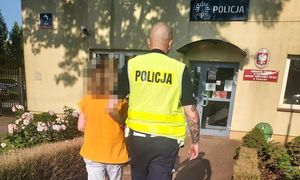 zatrzymana kobieta w asyście umundurowanego funkcjonariusza Policji, w tle budynek Komisariatu Policji w Lesznowoli