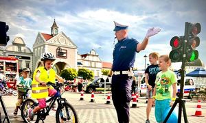 policjant kierujący ruchem na miasteczku ruchu drogowego, dzieci jeżdżące na rowerach