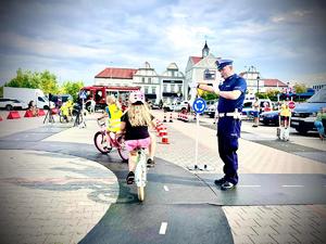 policjant kierujący ruchem na miasteczku ruchu drogowego, dzieci jeżdżące na rowerach