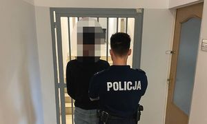 umundurowany policjant oraz zatrzymany mężczyzna na tle pomieszczenia dla osób zatrzymanych