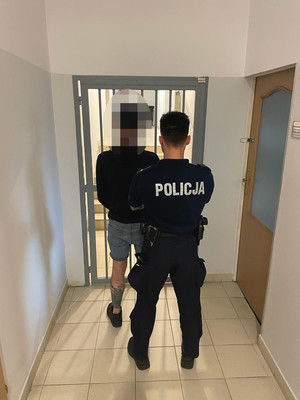 umundurowany policjant oraz zatrzymany mężczyzna na tle pomieszczenia dla osób zatrzymanych