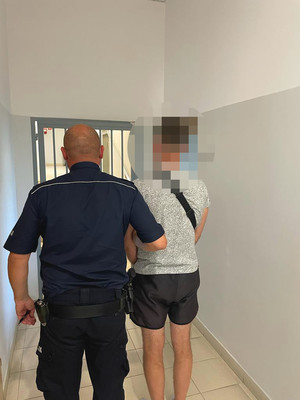 umundurowany policjant oraz zatrzymany mężczyzna na tle pomieszczenia dla osób zatrzymanych