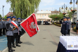 Na placu stoją umundurowani policjanci, którzy pochylają sztandar, przed którym komendant powiatowy policji oddaje honor.