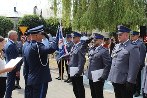 Umundurowany policjant stojący w szyku z innymi oddaje honor swoim przełożonym, którzy również oddają mu honor.