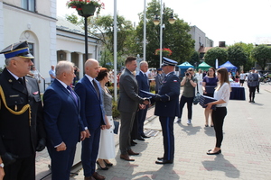 Umundurowany policjant wręcza przybyłom gościom podziękowania.