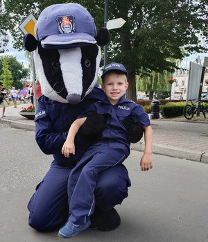 Na zdjęciu jest duża maskotka w stroju policyjnym, która trzyma chłopca w przebraniu policjanta.