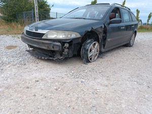 Na zdjęciu jest granatowe auto, które nie ma lewej opony, tylko gołą felgę. Pojazd nie ma też części przedniej karoserii, widać ślady uszkodzeń.