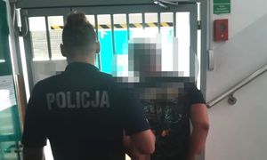 zatrzymany mężczyzna w asyście umundurowanego policjanta na tle drzwi wejściowych