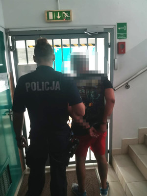 zatrzymany mężczyzna w asyście umundurowanego policjanta na tle drzwi wejściowych