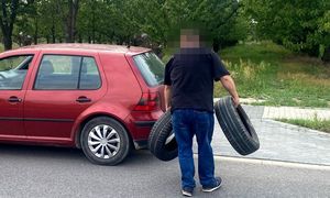 mężczyzna niosący dwie opony, w tle auto koloru bordowego