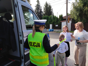 Na zdjęciu jest umundurowana policjantka z ruchu drogowego,która wręcza odblaski dzieciom.
