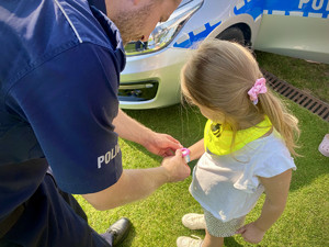 umundurowany policjant zakładający dziecku opaskę niezgubkę