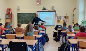 umundurowany policjant w trakcie zajęć, dzieci siedzą w ławkach