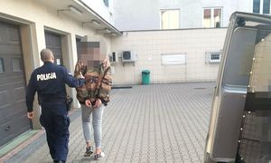zatrzymany mężczyzna w asyście umundurowanego policjanta idący na dziedzińcu komendy