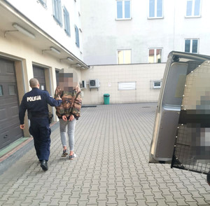 zatrzymany mężczyzna w asyście umundurowanego policjanta idący na dziedzińcu komendy
