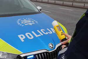 radiowóz policyjny oraz policjant z urządzeniem do sprawdzania stanu trzeźwości kierujących