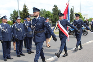 Przed szykiem umundurowanych policjantów idzie poczet flagowy, który niesie sztandar Komendy Powiatowej Policji Piasecznie.