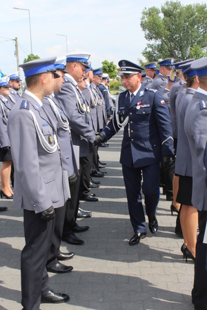 Umundurowany policjant idzie w rzędzie pomiędzy innymi policjantami i składa gratulacje.