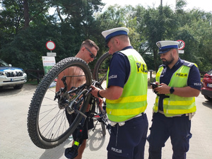 Policjanci z ruchu drogowego sprawdzają oznakowanie roweru, który trzyma inny  mężczyzna.