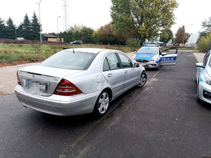 srebrny mercedes zatrzymany do kontroli drogowej, w tle policyjny radiowóz z włączonymi sygnałami świetlnymi