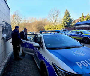 zatrzymany mężczyzna wsiadający do policyjnego radiowozu, obok umundurowany policjant