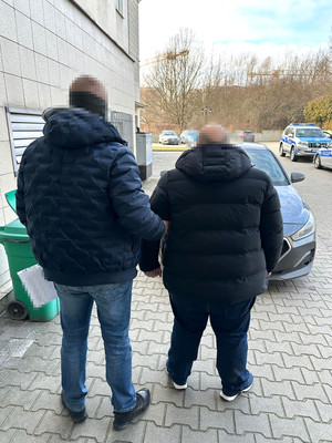 zatrzymany mężczyzna wraz z nieumundurowanym policjantem, w tle policyjne radiowozy