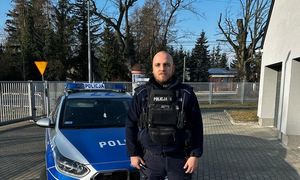umundurowany policjant, stojący przy zaparkowanym radiowozie