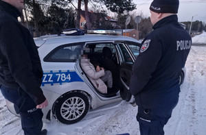 policjanci stojący przy radiowozie w którym siedzi odnaleziona kobieta