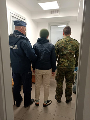 zatrzymany mężczyzna w asyście policjanta oraz funkcjonariusza straży granicznej