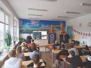 zdjęcie ze spotkania z uczniami, młodzież siedzi w ławkach szkolnych, przed nimi stoją umundurowani policjanci