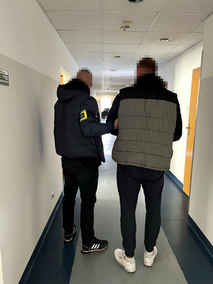 poszukiwany mężczyzna w asyście nieumundurowanego policjanta stojący na korytarzu